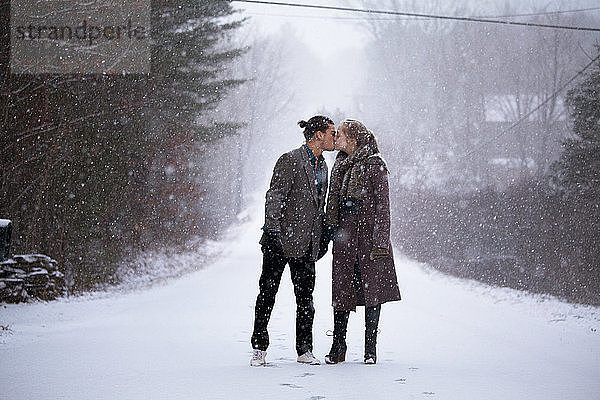 Romantisches Paar küsst sich im Stehen auf verschneitem Feld bei Schneefall