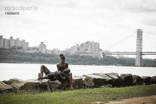 Ehepaar entspannt sich auf Felsen am Flussufer vor Brücke