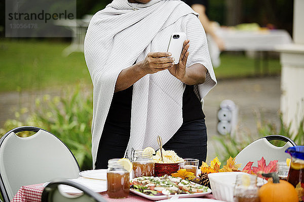 Mitschnitt einer Frau  die am Tisch stehend am Telefon Essen fotografiert