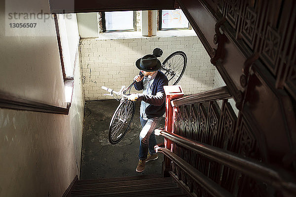 Hochwinkelansicht eines Mannes  der zu Hause beim Treppensteigen ein Fahrrad trägt