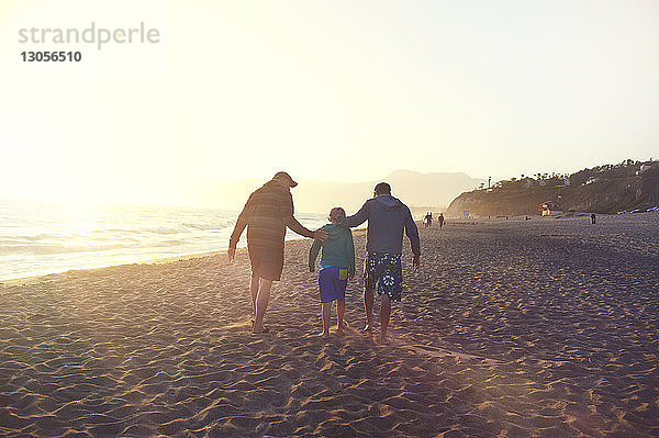 Rückansicht einer Familie  die bei Sonnenuntergang am Strand bei klarem Himmel spazieren geht