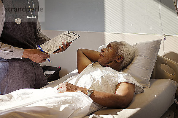 Älterer Mann sieht Arzt an  während er im Krankenhaus auf dem Bett liegt