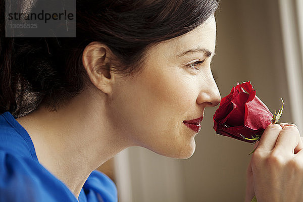 Nahaufnahme einer Frau  die an einer roten Rose riecht