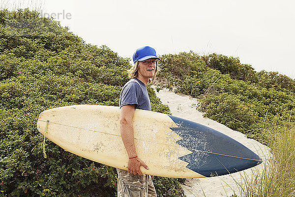 Porträt eines glücklichen Mannes mit Surfbrett vor klarem Himmel