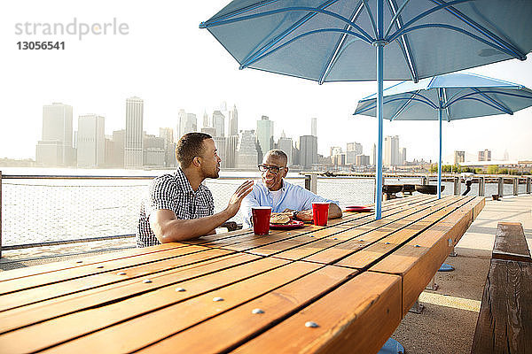 Sohn spricht mit Vater  während er in der Stadt am East River am Tisch sitzt