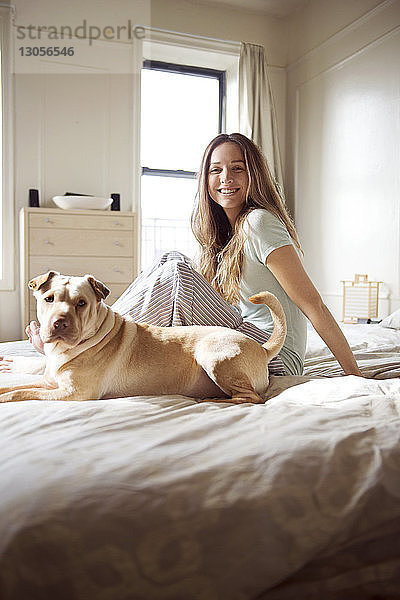 Porträt einer glücklichen Frau mit Hund auf dem Bett