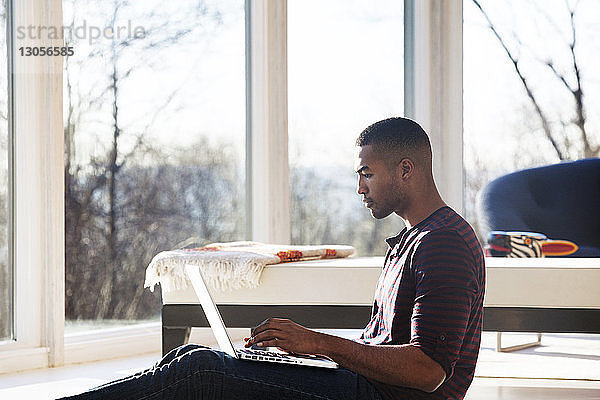 Mann benutzt Laptop-Computer  während er zu Hause sitzt