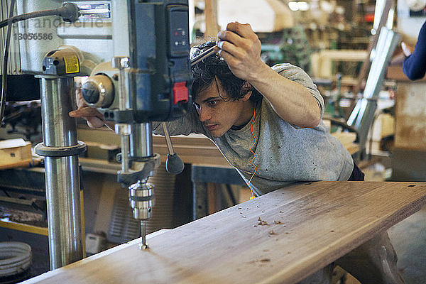 Männlicher Zimmermann mit Maschinen auf Holzbrettern in der Werkstatt