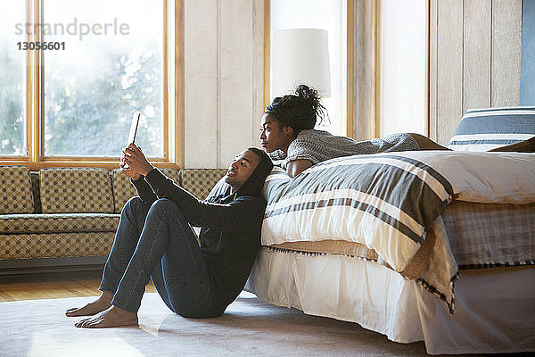 Ehepaar betrachtet Tablet-Computer  während es sich im Schlafzimmer entspannt