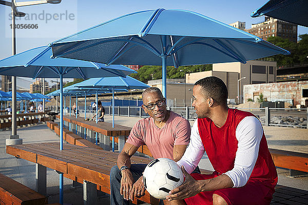 Vater spricht mit Mann  der einen Fussball hält  während er am Tisch sitzt
