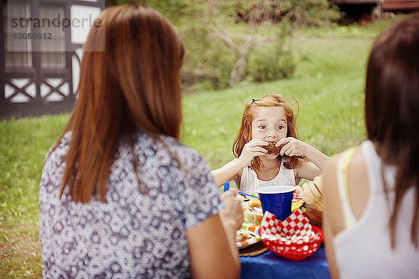 Mädchen isst Essen  während sie mit der Familie am Picknicktisch sitzt