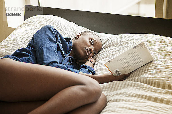 Frau liest Buch  während sie zu Hause im Bett liegt