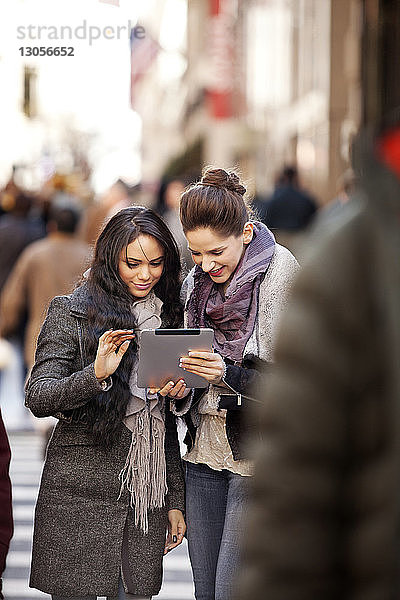 Glückliche Freundinnen schauen auf das digitale Tablet  während sie auf der Straße stehen