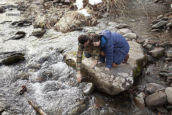 Paar berührt Flusswasser  während es auf einem Felsen kniet