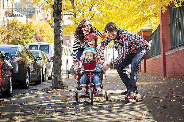 Glückliche Familie geniesst Skateboard und Dreirad auf dem Fussweg