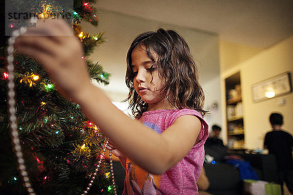 Mädchen schmückt den Weihnachtsbaum zu Hause