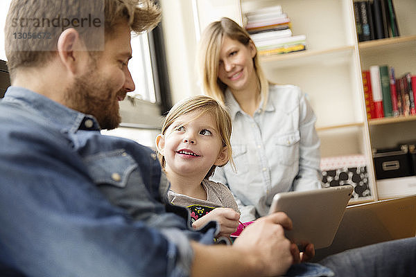 Mädchen sieht Vater mit digitalem Tablet und Frau im Hintergrund