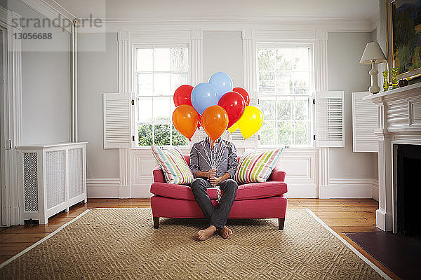 Mann hält Heliumballons  während er zu Hause auf dem Sofa sitzt