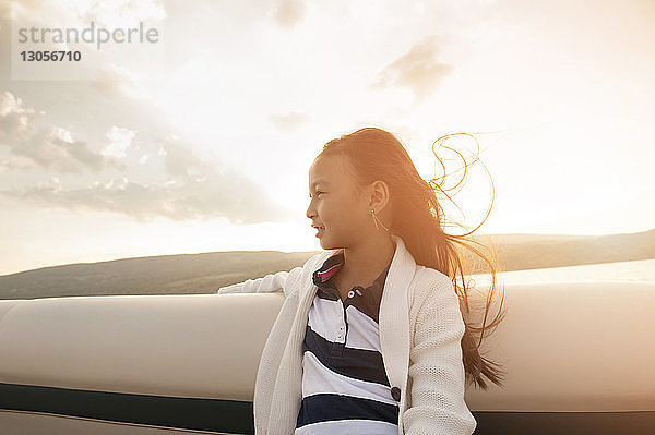 Mädchen schaut weg  während sie bei Sonnenuntergang im Boot gegen den Himmel sitzt