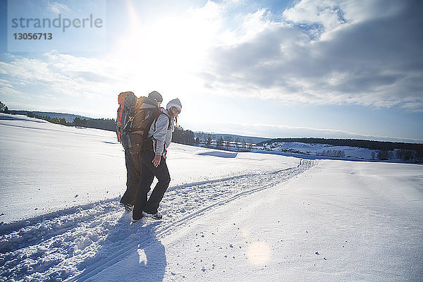 Freunde tragen Rucksack beim Wandern auf schneebedecktem Feld gegen bewölkten Himmel