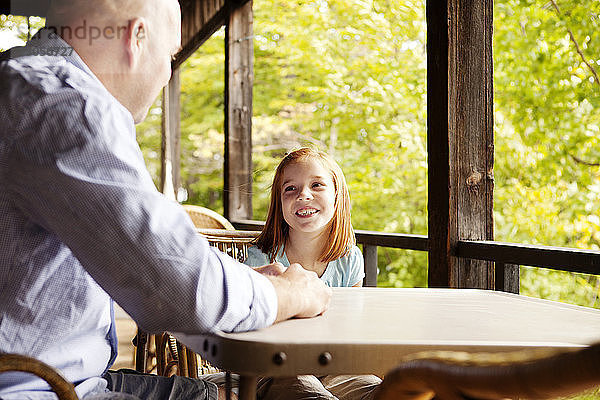 Glückliches Mädchen unterhält sich mit dem Vater  während sie im Pavillon am Tisch sitzt