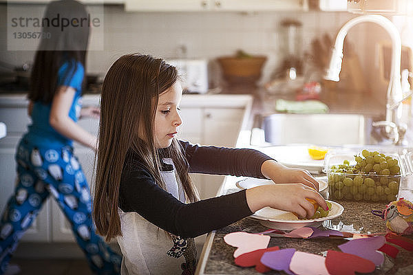 Mädchen nimmt Trauben an der Küchentheke von Schwester zu Hause