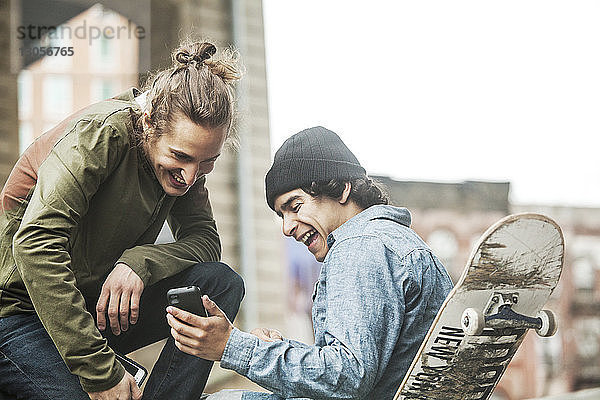 Glückliche Freunde schauen auf Smartphone im Skateboard-Park