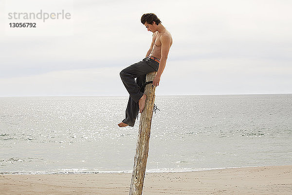 Mann ohne Hemd auf Holzpfosten am Strand sitzend