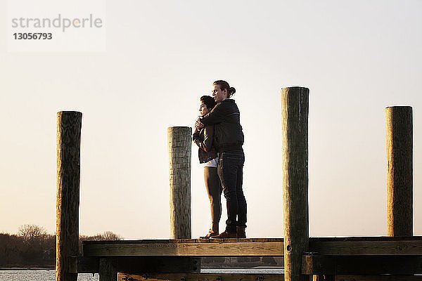 Ehepaar steht bei Sonnenuntergang am Pier gegen den Himmel