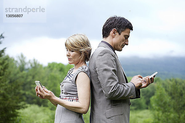 Seitenansicht eines Paares  das ein Mobiltelefon benutzt  während es gegen den Himmel steht