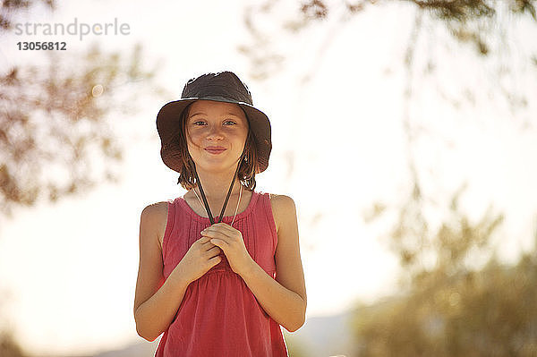 Porträt eines glücklichen Mädchens mit Hut  das an einem sonnigen Tag am Himmel steht