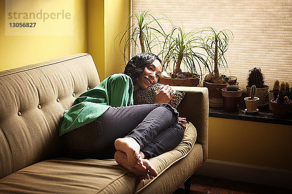 Lächelnde Frau schaut weg  während sie sich zu Hause auf dem Sofa entspannt