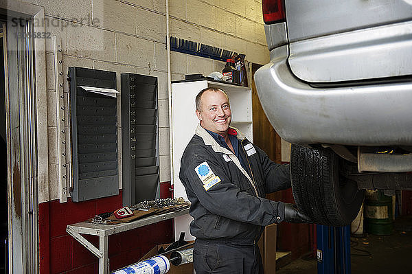 Porträt eines glücklichen Mechanikers  der in einer Autowerkstatt arbeitet