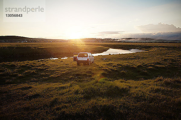 Bei Sonnenuntergang auf dem Feld am Fluss geparktes Auto