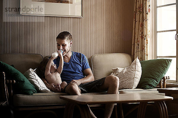 Verspielter Sohn füttert den Vater  während er zu Hause auf dem Sofa sitzt