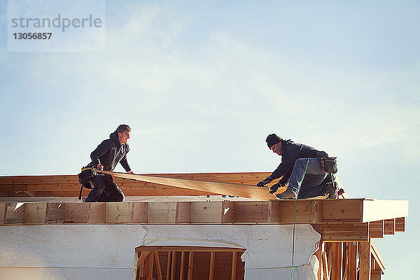 Arbeiter  die bei Sonnenschein Dachbalken gegen den Himmel konstruieren