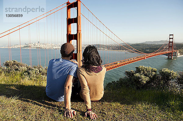 Rückansicht eines jungen Paares  das sich auf dem Spielfeld gegen die Golden Gate Bridge entspannt
