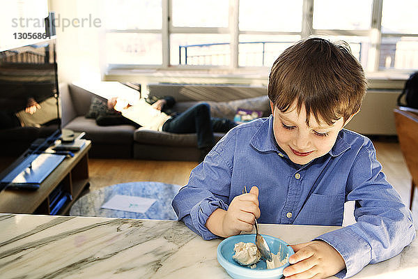 Glücklicher Junge isst zu Hause Eiscreme in Schüssel
