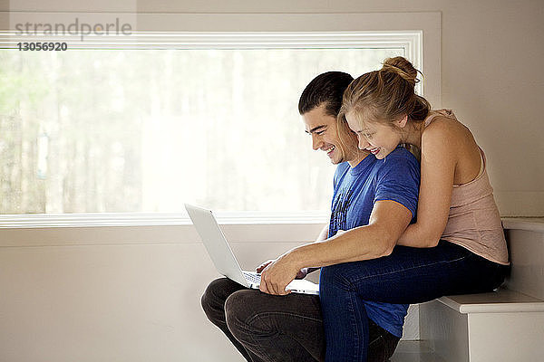Glückliches Paar benutzt Laptop-Computer  während es zu Hause auf Stufen sitzt