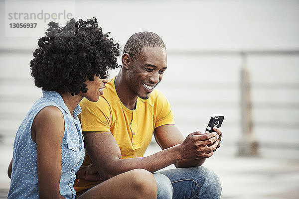 Paar  das auf der Promenade sitzend auf ein Mobiltelefon schaut
