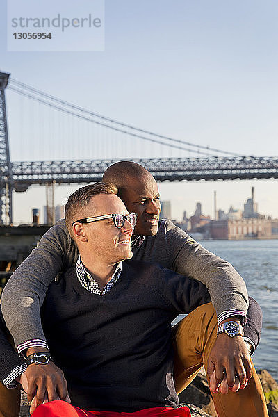 Romantische Freunde schauen auf East River  während sie gegen die Williamsburg Bridge sitzen