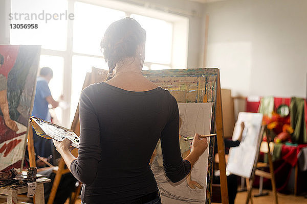 Rückansicht einer Frau beim Malen im Stehen im Kunstunterricht