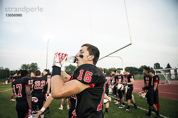 Junge trinkt Wasser auf American-Football-Feld gegen den Himmel