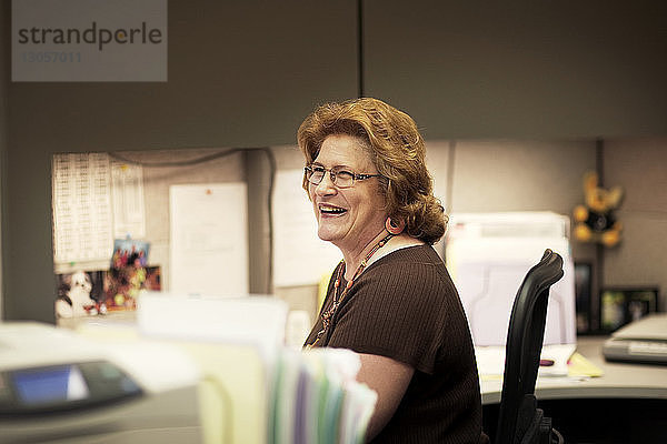 Lächelnde Frau schaut weg  während sie im Büro sitzt