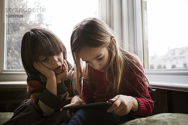 Junge sieht Schwester an  die zu Hause einen Tablet-Computer benutzt