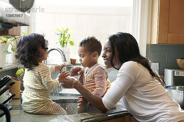 Mutter sieht Kinder an  die in der Küche mit Wasser in der Spüle spielen