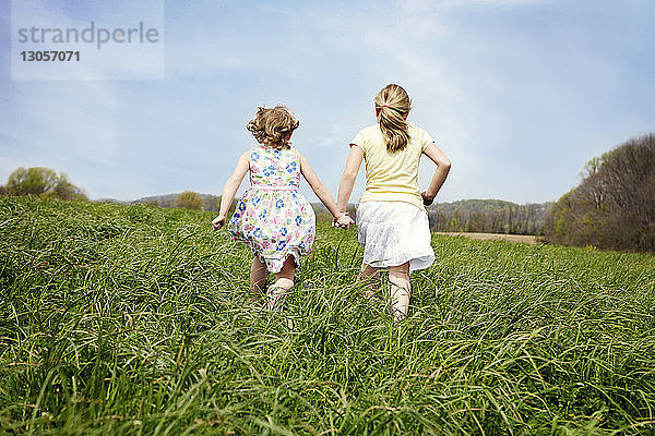 Rückansicht von Mädchen  die auf einem Grasfeld gegen den Himmel laufen