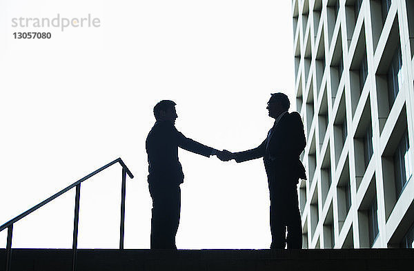 Silhouette von Geschäftsleuten  die dem Himmel die Hand schütteln