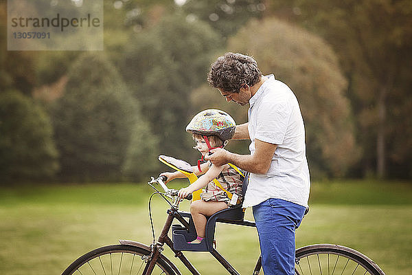 Vater befestigt den Helm einer Tochter  die im Park auf dem Fahrrad sitzt