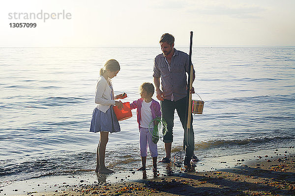 Vater hält Reinigungsgerät in der Hand  während er mit den Töchtern am Ufer steht